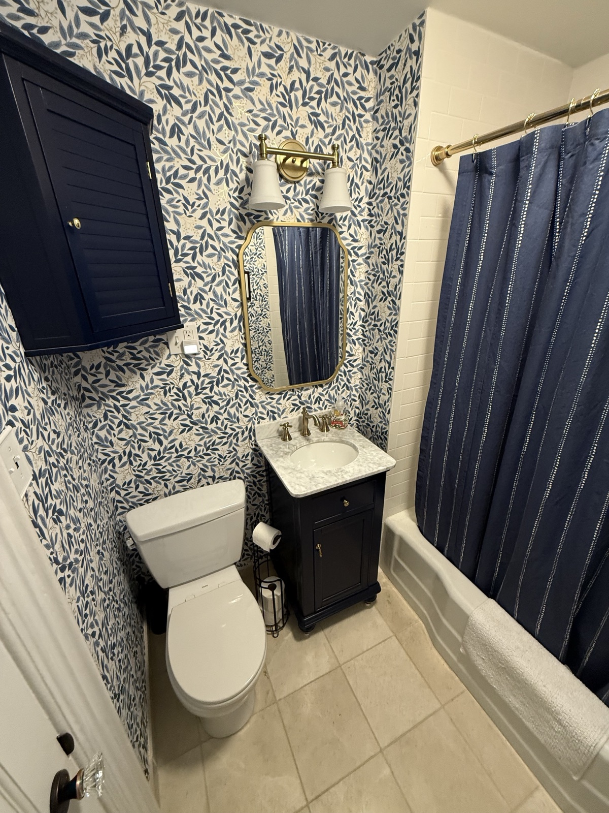 Small bathroom with blue botanical wallpaper, a navy vanity with a marble top, and a toilet